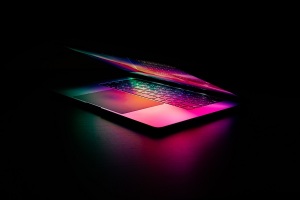 Photo of a glowing, half-closed laptop in a dark room.