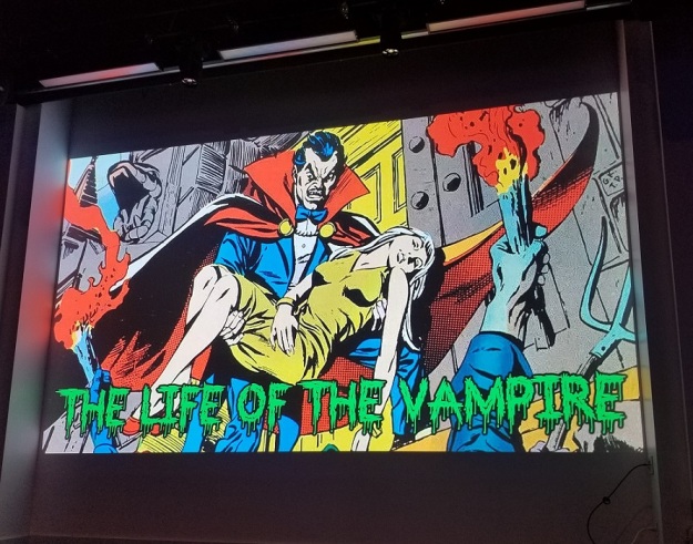 A comic book image of a vampire carrying a woman through city streets.